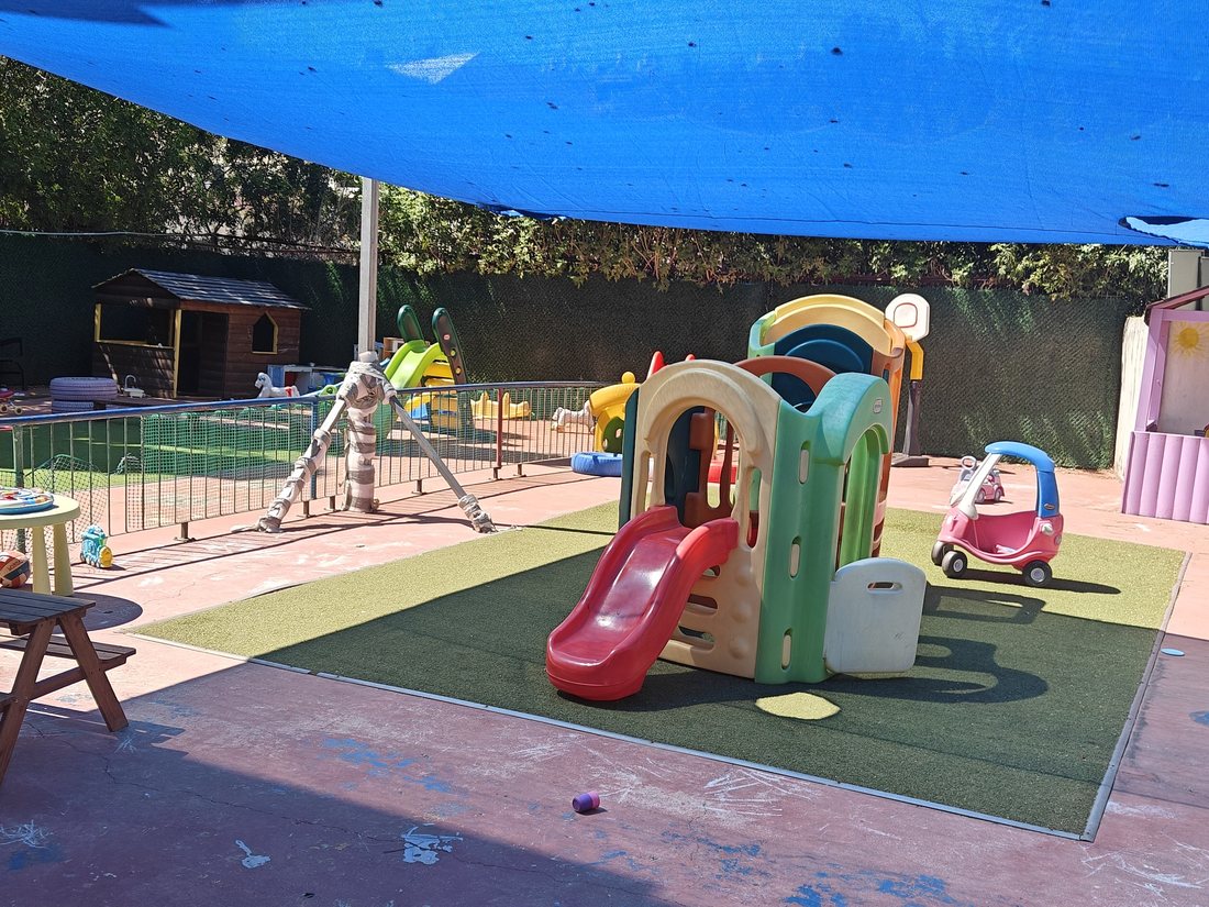 החצר של הדבורה מאיה — דשא סינתטי, מתקן טיפוס עם מגלשה ורשת הצללה על כל השטח