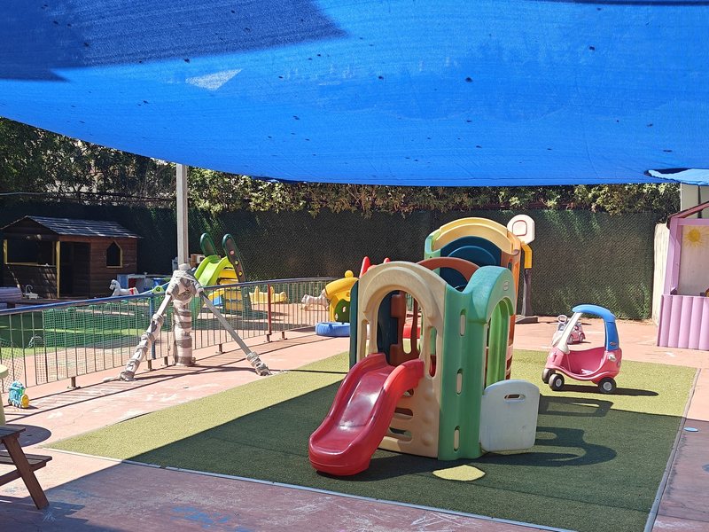 מבט רחב על החצר — מתקן הטיפוס, שולחן פיקניק ובתי משחק