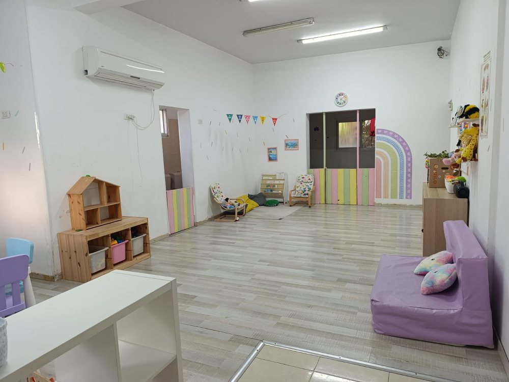 חדר קבוצת 2–3 — שולחן פעילות, כיסאות אוכל וחלון לחצר